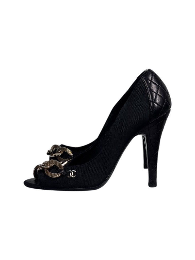 Black Chanel shoes with gold chain detail on a white background