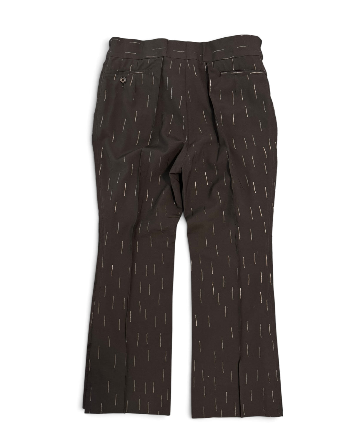 Black wide-leg CCOMME DES GARCONS trousers with a subtle vertical dash pattern, laid flat on a textured gray background.