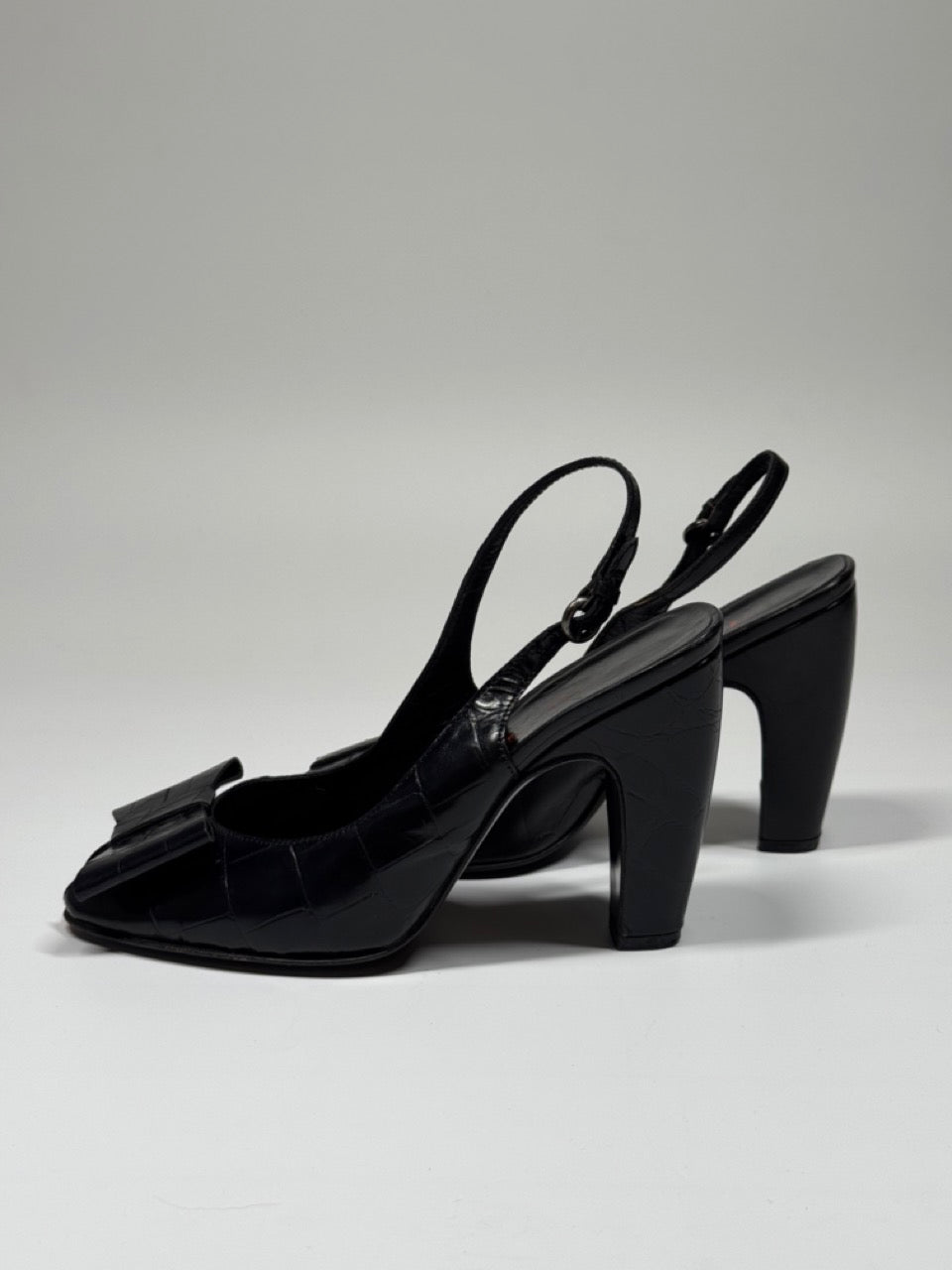 Pair of black high-heeled shoes with bow detail on a light gray background