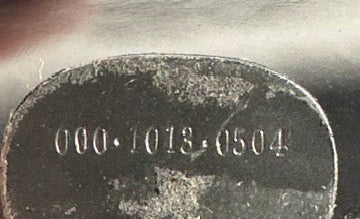 Close-up of a metallic object with engraved numbers, held by a person's hand.