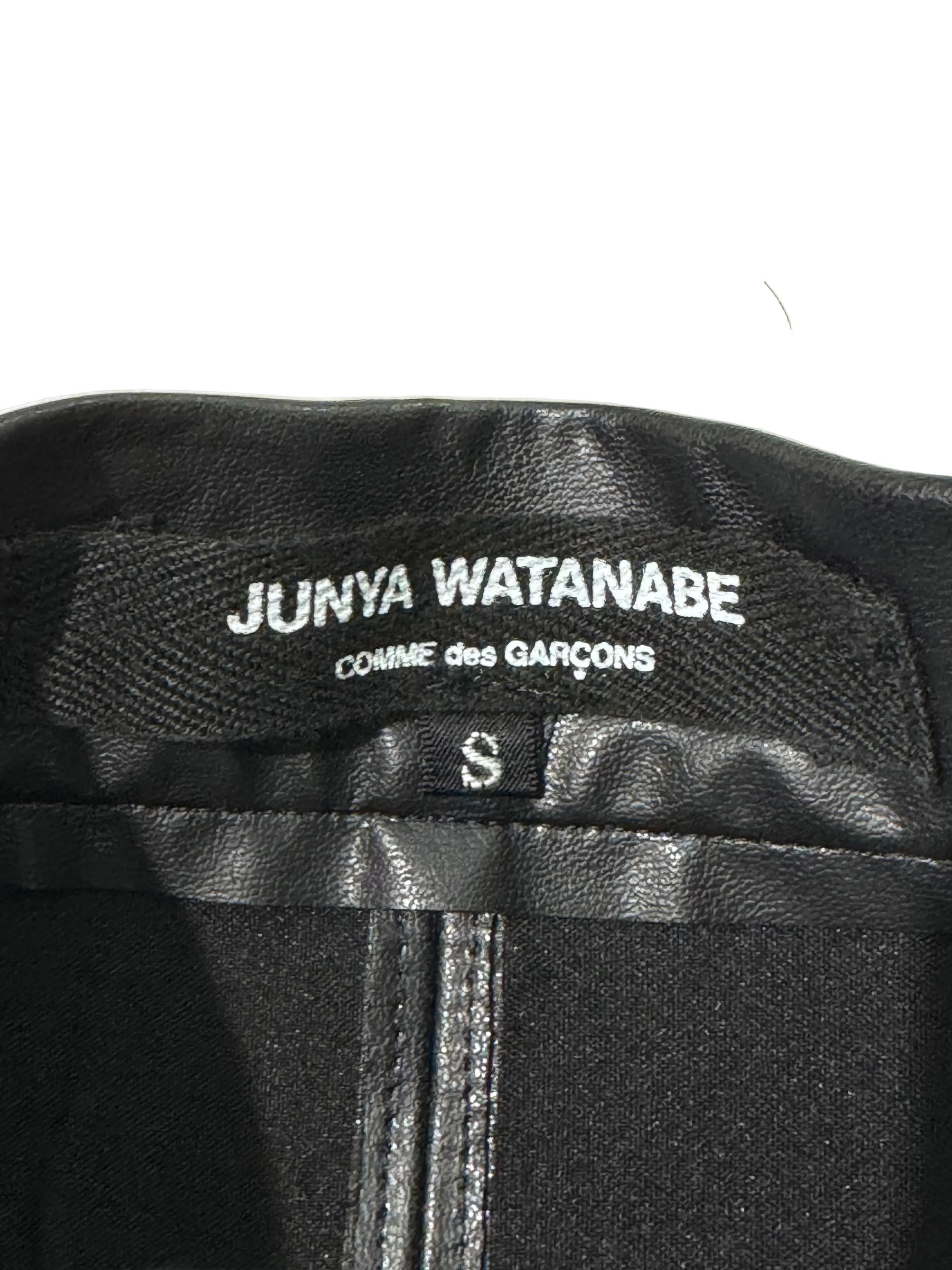Black leather shorts with Junya Watanabe label on a textured beige background