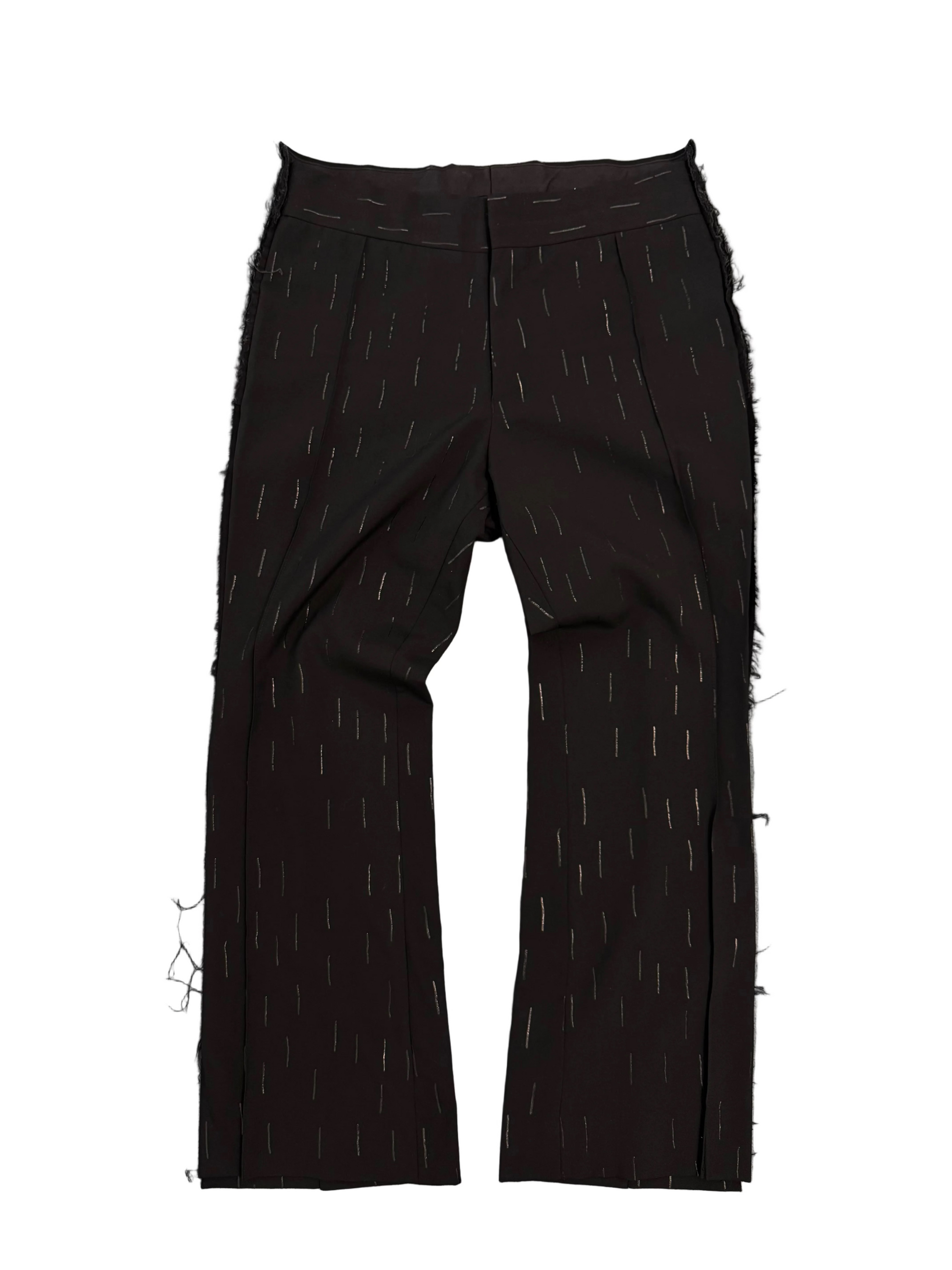 Black wide-leg CCOMME DES GARCONS trousers with a subtle vertical dash pattern, laid flat on a textured gray background.