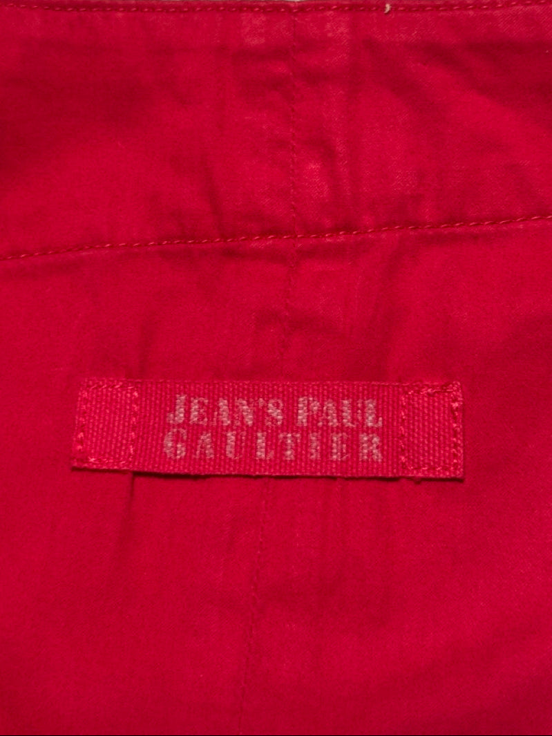 Red fabric with a 'Jean Paul Gaultier' label on a textured gray background