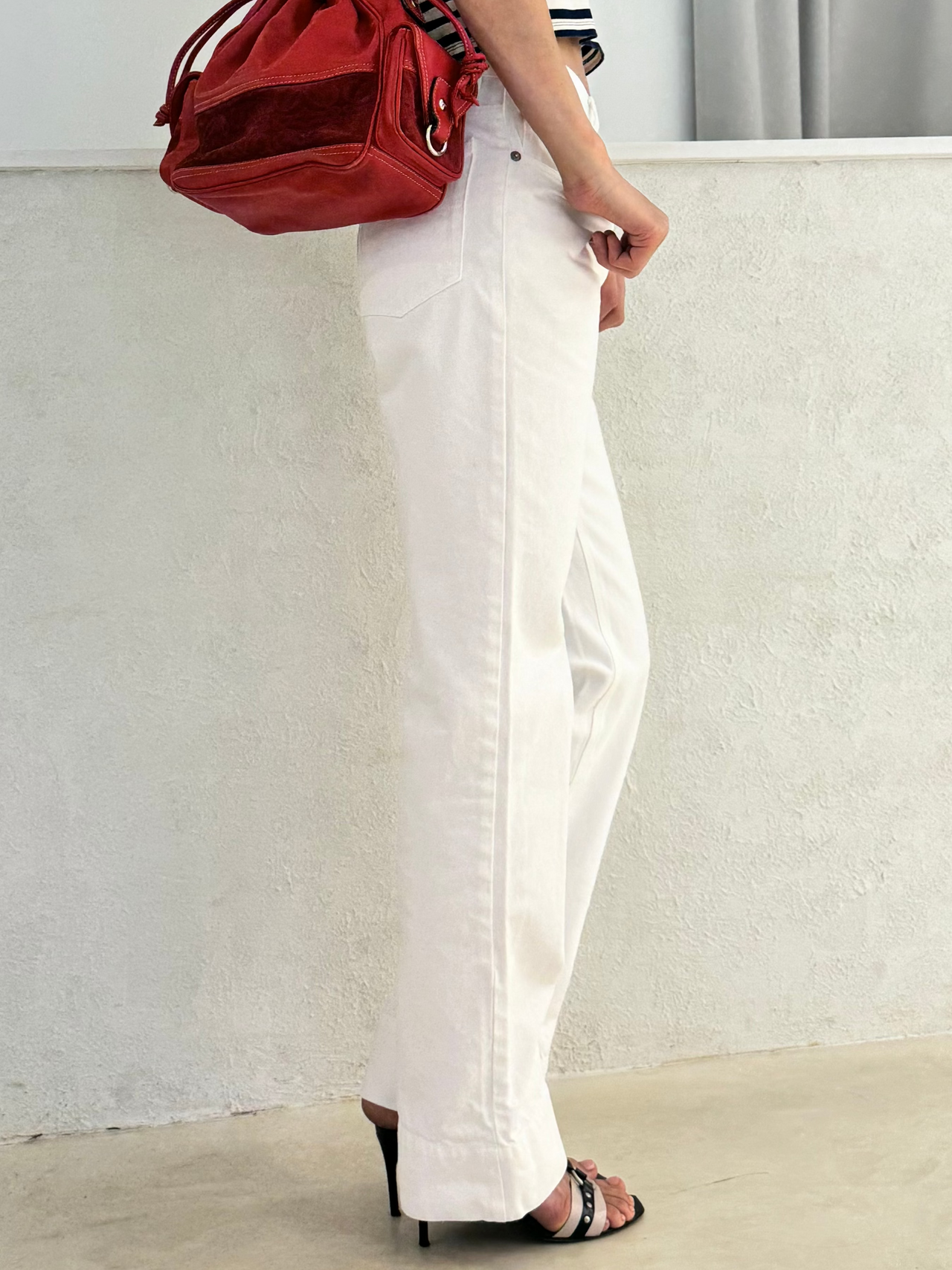 Woman in a striped shirt and white dries van noten pants holding a red bag against a plain background