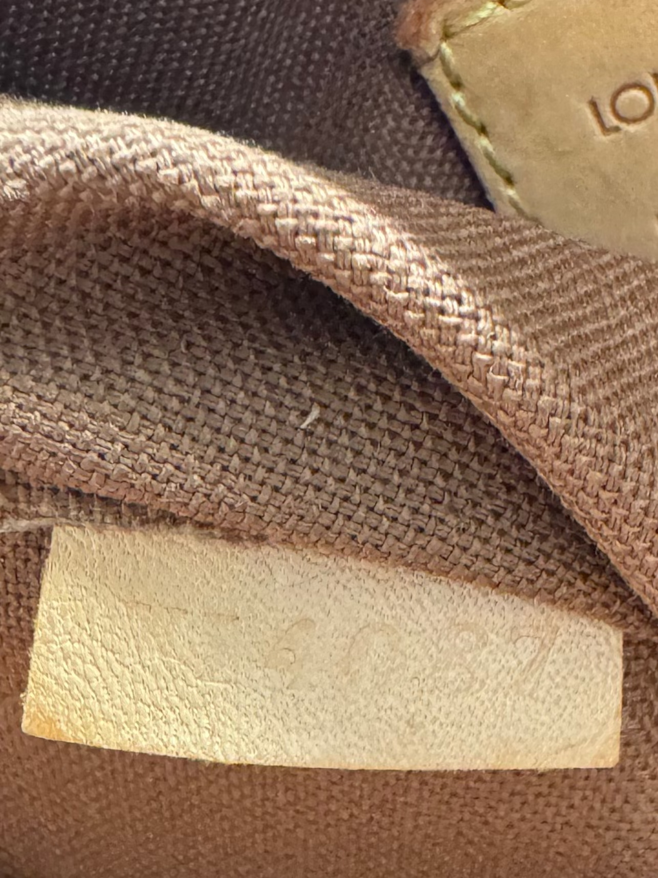 Close-up of the interior of a Louis Vuitton bag, showing the brown canvas material and a tan leather brand label that reads 'LOUIS VUITTON PARIS made in France'. A hand with a French manicure is holding the opening.