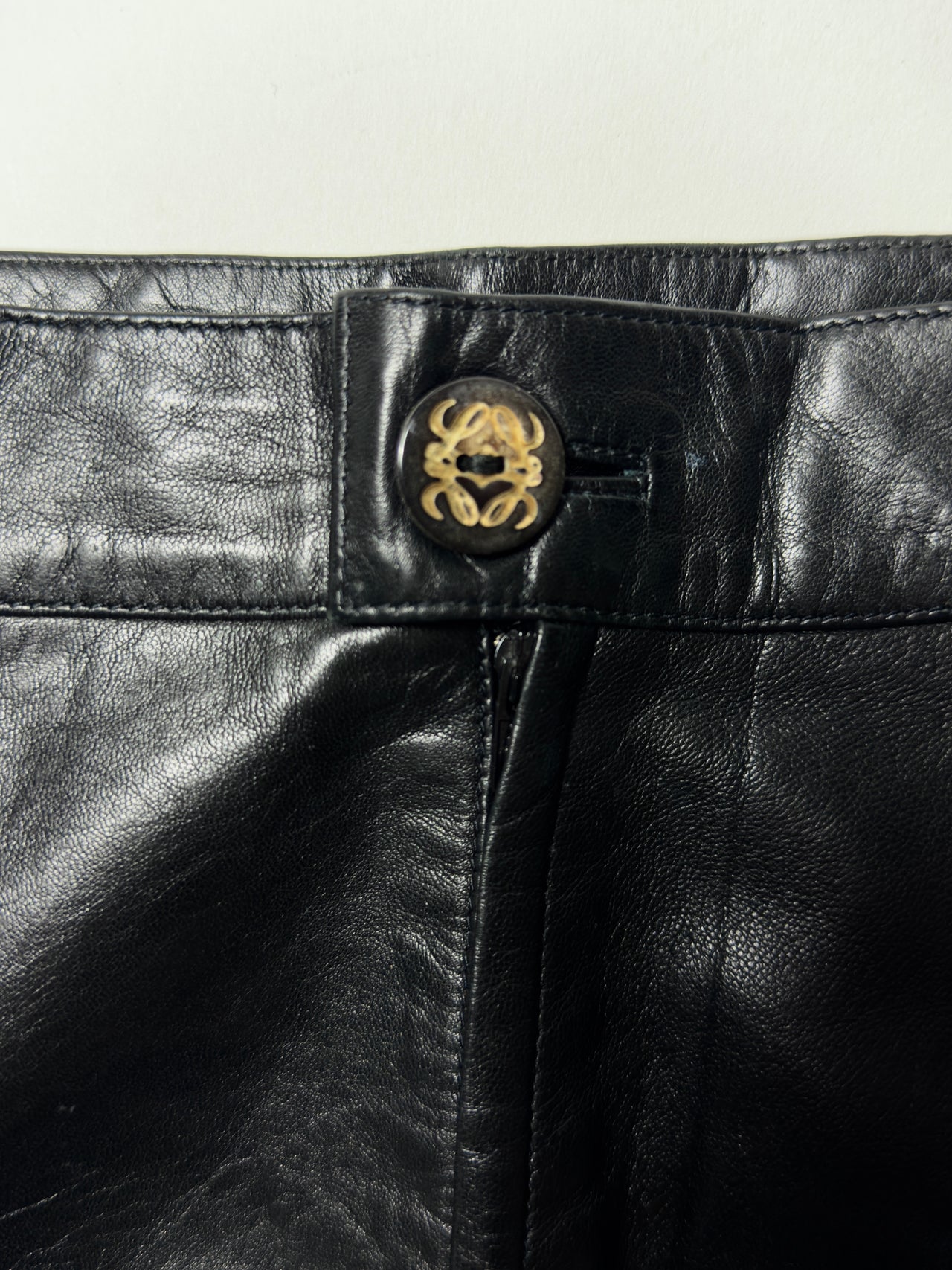 A black leather pencil skirt with a button at the front, featuring a swerve design on the front and back.