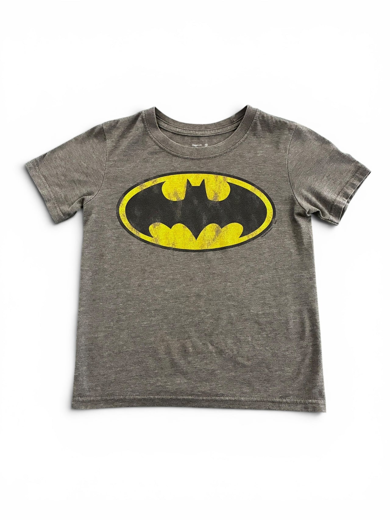 A person taking a mirror selfie in a fitting room wearing a gray cropped t-shirt with a yellow Batman logo and black track pants with white side stripes.