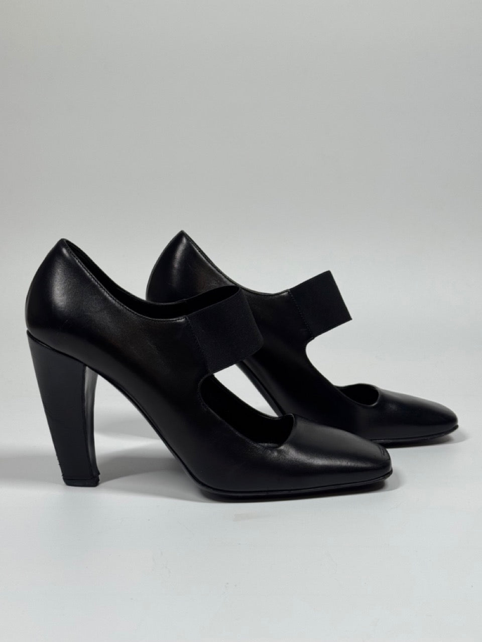 Black high-heeled shoes with a strap on a gray background