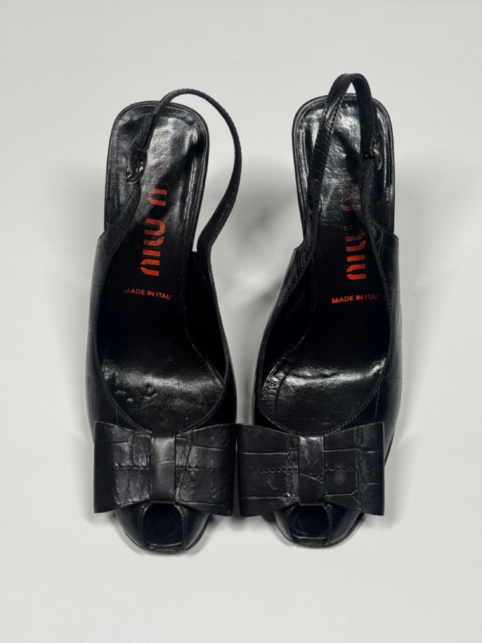 Pair of black high-heeled shoes with bow detail on a light gray background