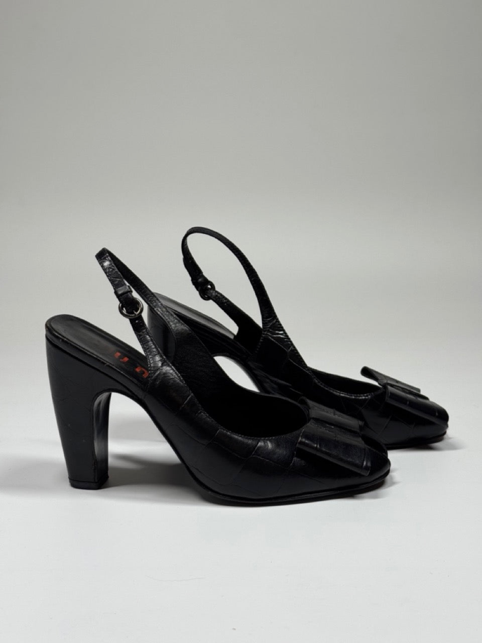 Black high-heeled shoes with bow details on a gray background