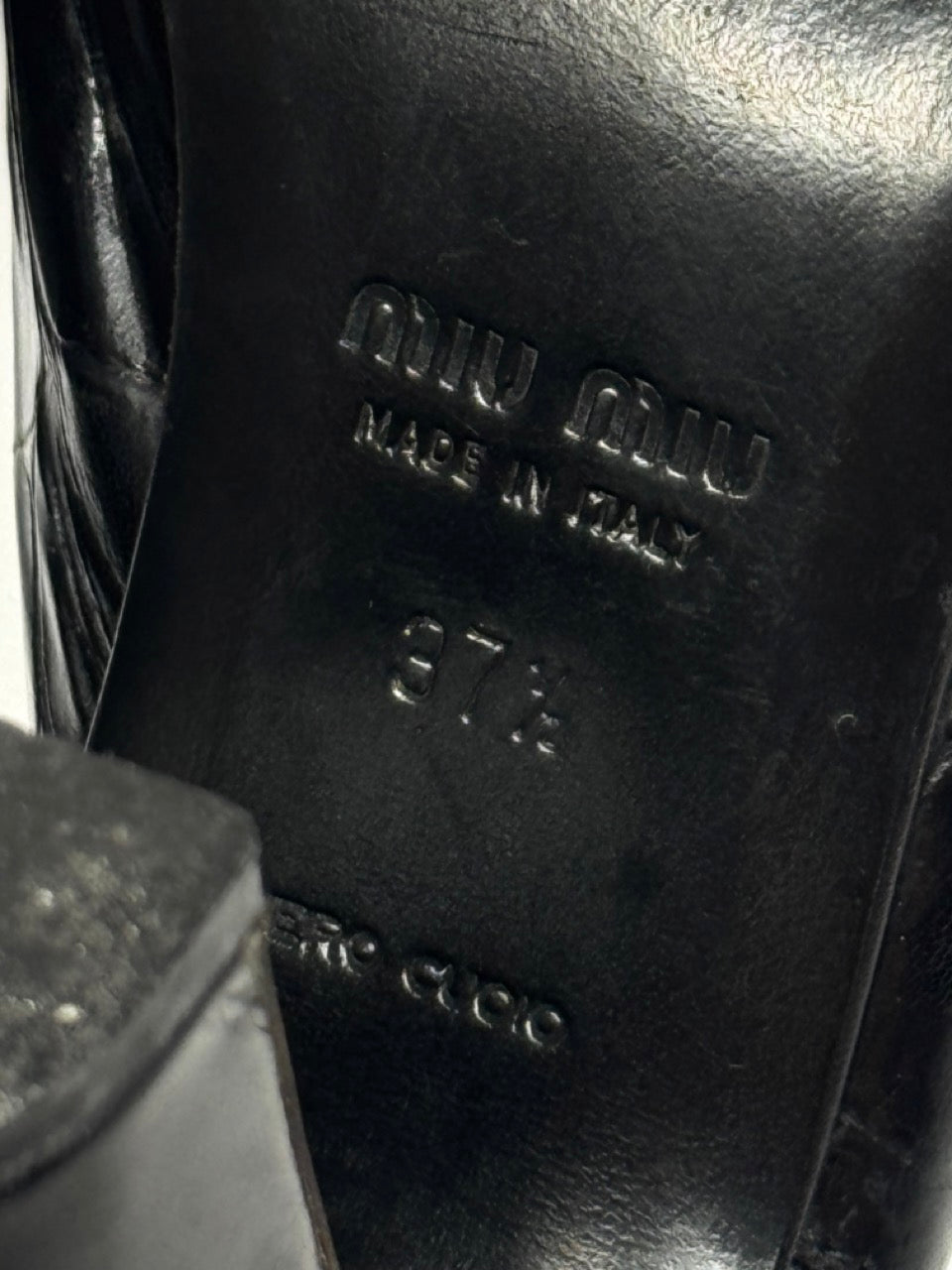 Close-up of a black leather shoe with 'Miu Miu' branding.
