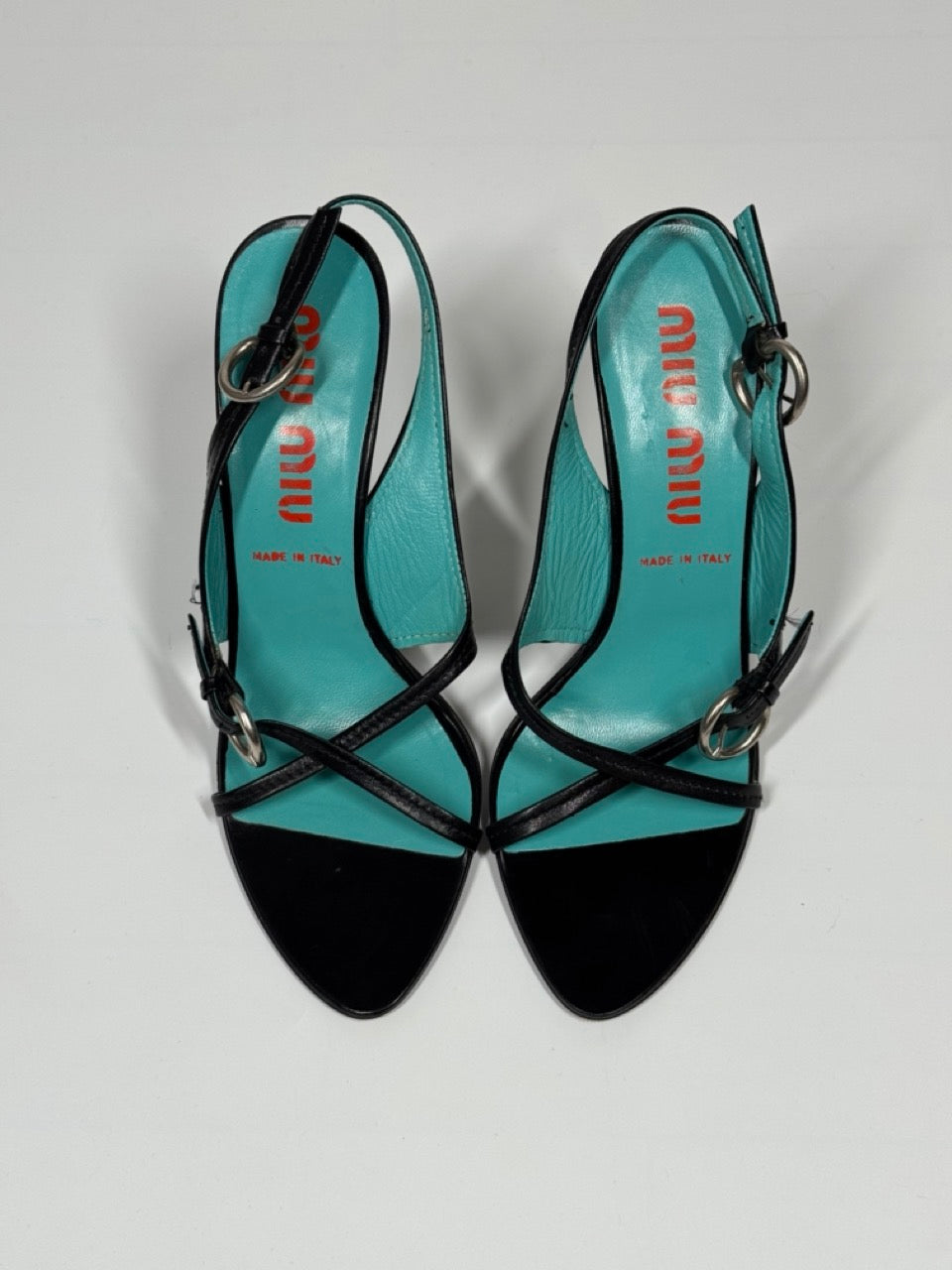 Pair of turquoise high-heeled shoes with black straps on a light gray background