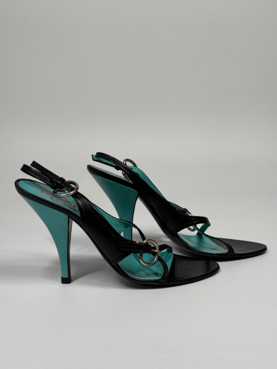 Pair of turquoise high-heeled shoes with black straps on a light gray background