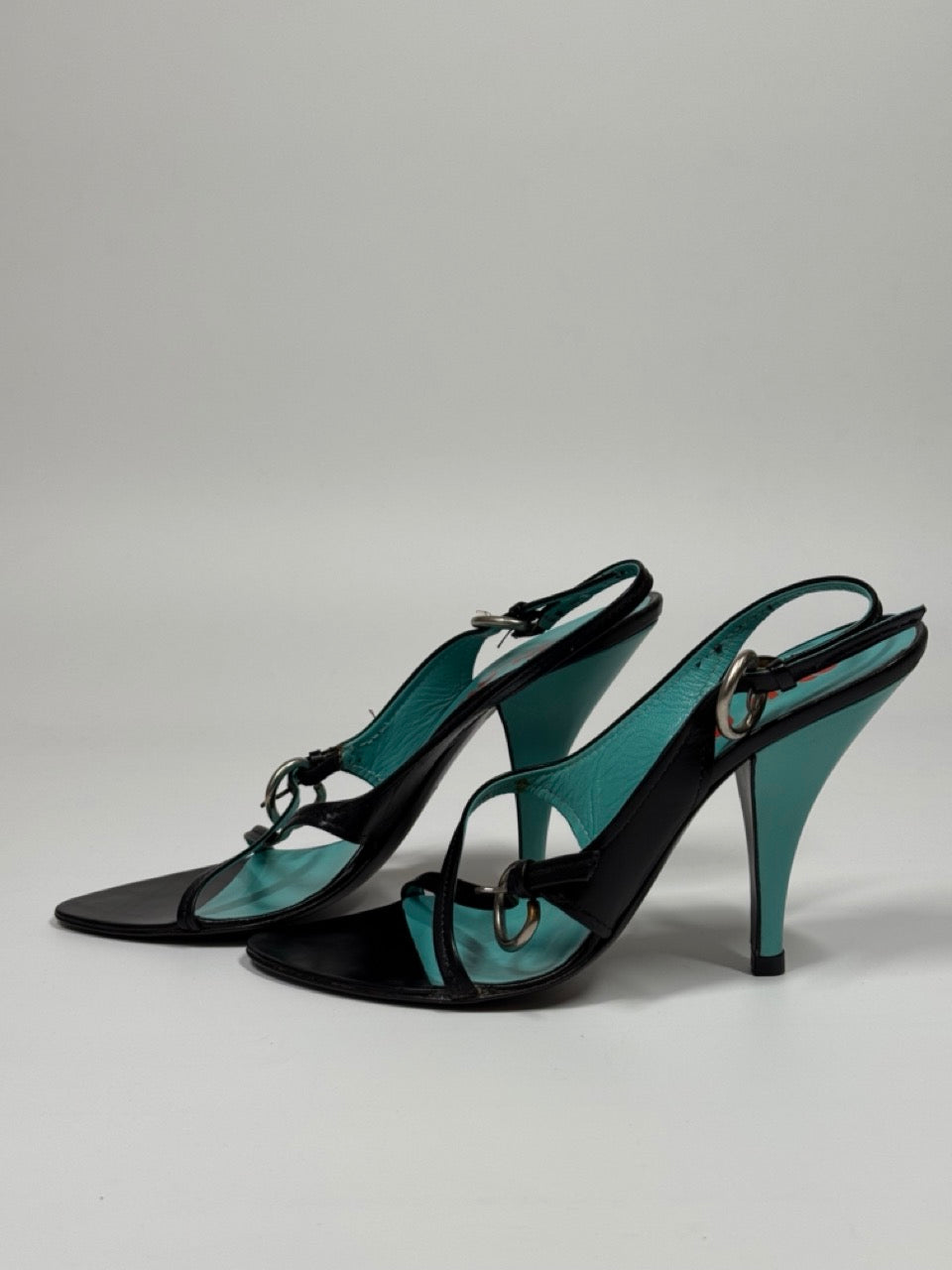 Pair of black high-heeled shoes with turquoise accents on a gray background