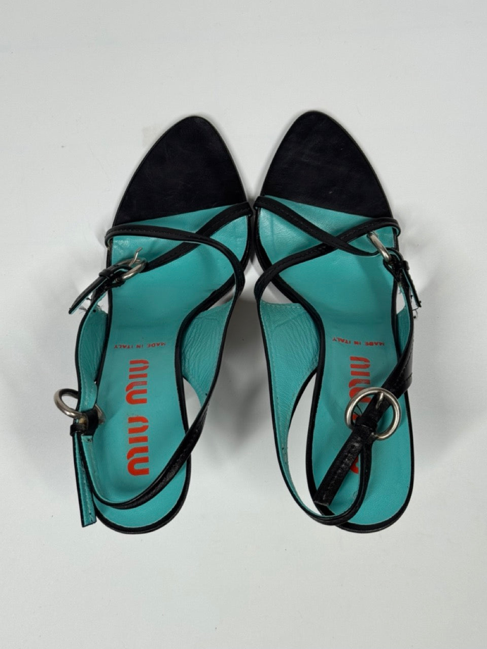 Pair of turquoise miu miu sandals with black straps on a light gray background