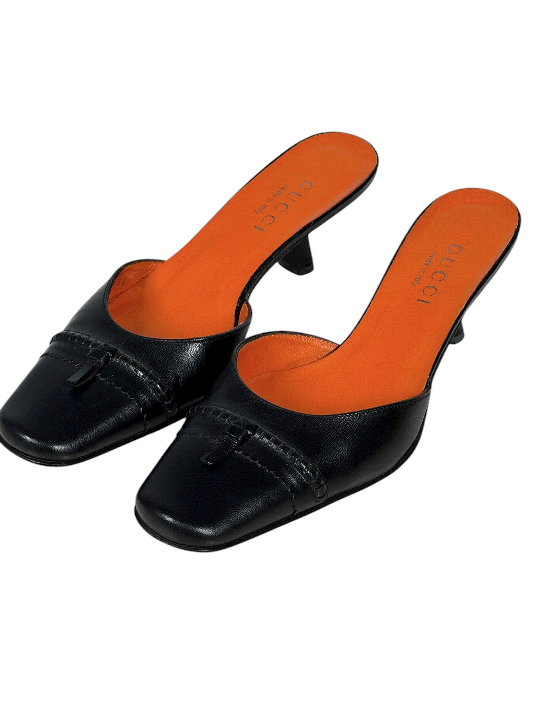 Black leather mules with orange insoles on a white background