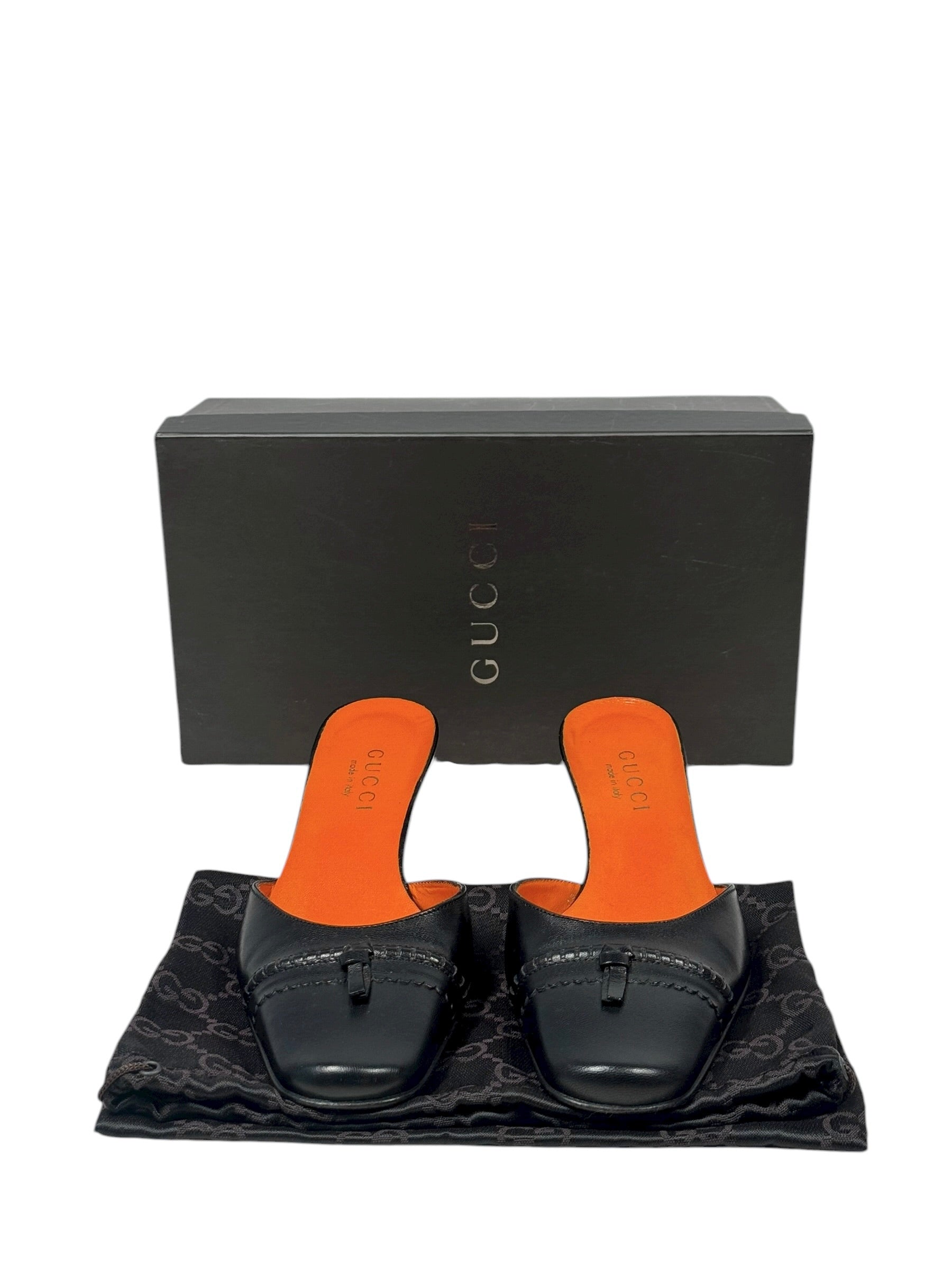 Black loafers with orange soles on a Gucci branded mat, with a black Gucci box in the background.