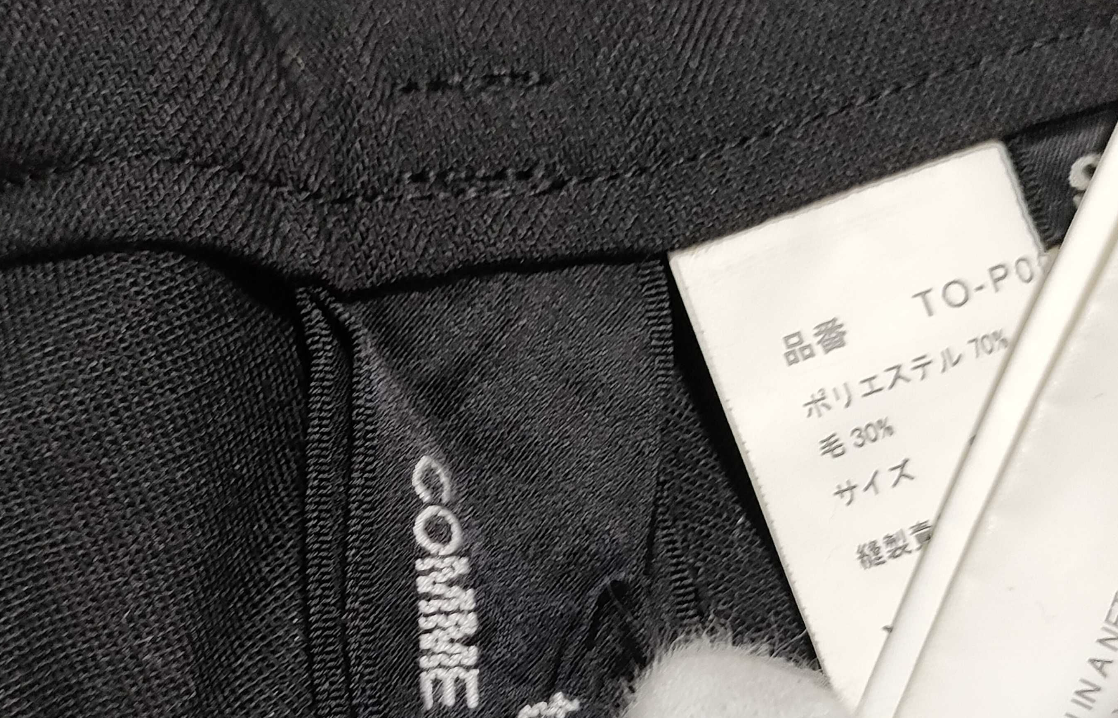 Close-up of black fabric with 'COMME' branding and a white label with text.