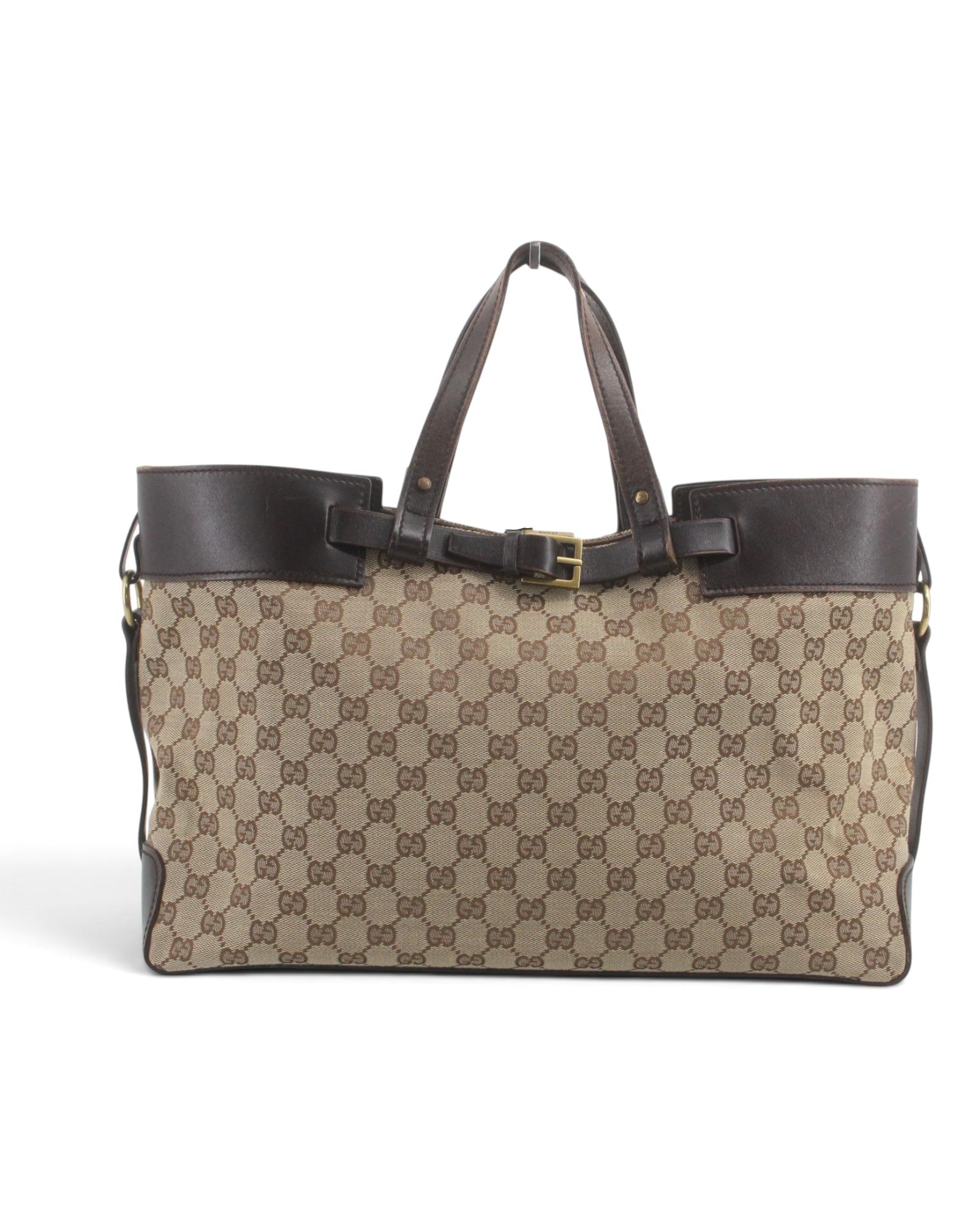 A Gucci tote bag in beige and brown GG Supreme canvas with dark brown leather trim, double top handles, and a central buckle detail, shown against a plain white background.
